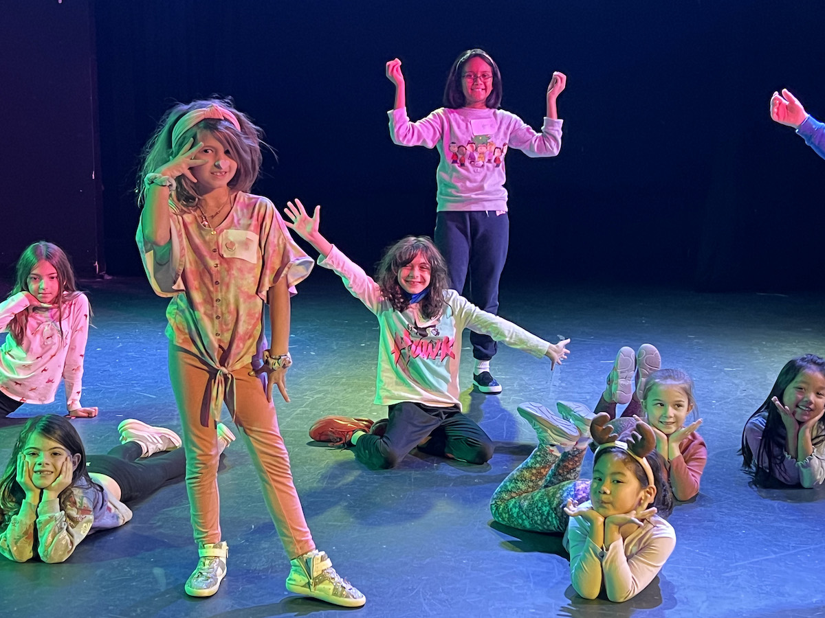 Students in theatre camp pose on stage with lights