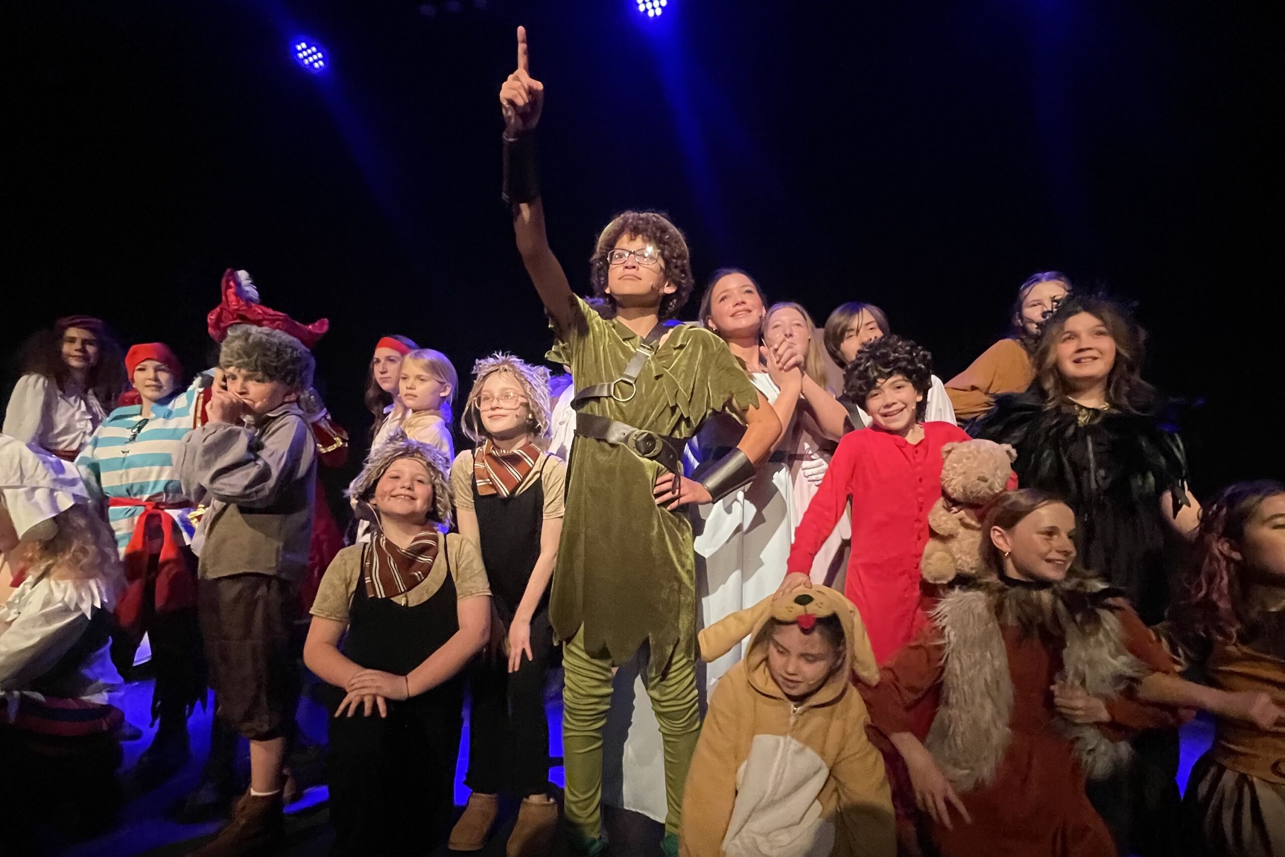 Child actor points up surrounded by castmates in performance of Peter Pan